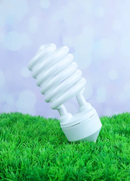 Energiesparlampe auf grünem Gras, auf hellem Hintergrund — Stockfoto