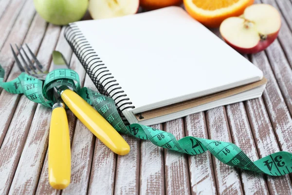 Besteck mit Maßband und Notizbuch mit Früchten auf Holzgrund gebunden — Stockfoto