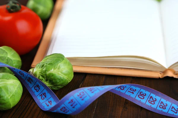 Livre avec ruban à mesurer et légumes sur fond en bois — Photo