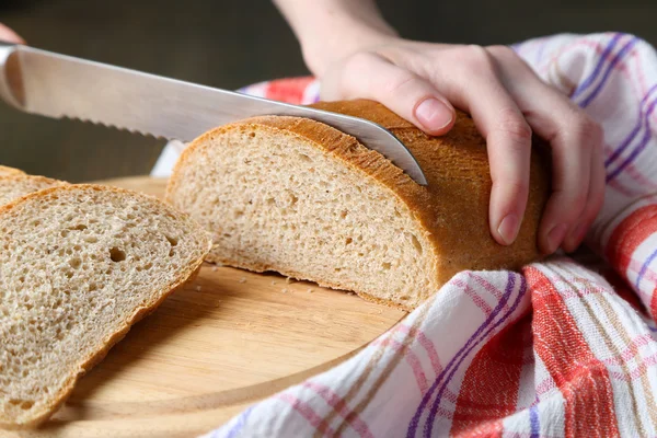 Mani femminili taglio del pane su tavola di legno, primo piano — Foto Stock