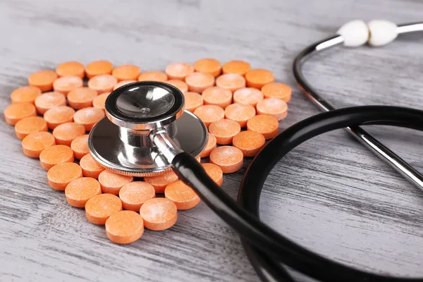 Cuore di pillole e stetoscopio su sfondo di legno — Foto Stock