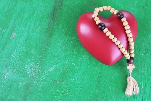 Corazón con rosario sobre fondo de madera — Foto de Stock