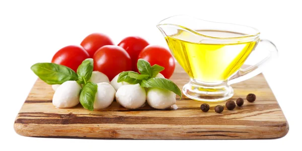 Composição com saborosas bolas de queijo mussarela, manjericão e tomates vermelhos, azeite sobre tábua de corte, isolado em branco — Fotografia de Stock