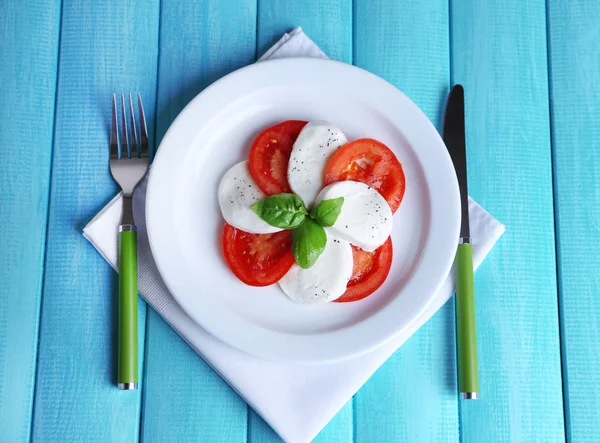 Caprese salade met mozarella kaas, tomaten en basilicum op plaat, op houten tafel achtergrond — Stockfoto