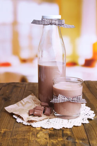Chocolate milk in bottle and glass, on wooden table, on bright background — Stock Photo, Image
