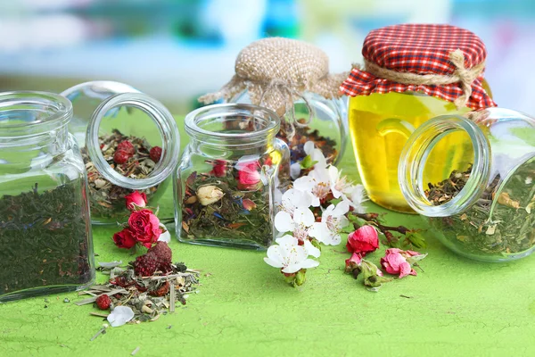 各式各样的草药和茶和蜂蜜在玻璃罐里的木桌前，在明亮的背景上 — 图库照片
