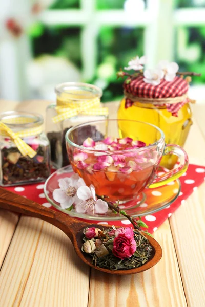 Assortment of herbs, honey and tea in glass jars on wooden table, on bright background — Stock Photo, Image