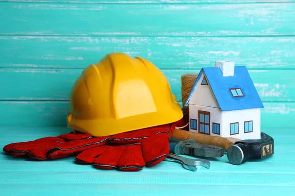 Composição com capacete de segurança, luvas de couro, ferramentas e casa decorativa em fundo de madeira — Fotografia de Stock