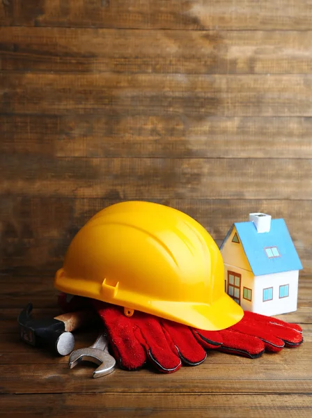 Composition with safety helmet, leather gloves, tools and decorative house on wooden background — Stock Photo, Image