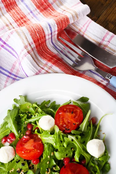 Groene salade gemaakt met rucola, tomaten, kaas mozzarella ballen en sesam op plaat, op houten achtergrond — Stockfoto