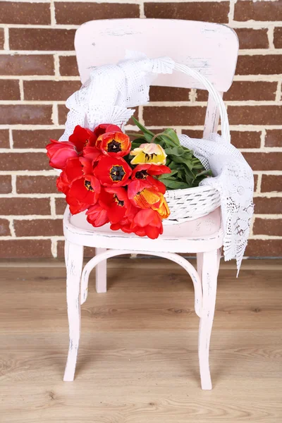 Bukiet kolorowych tulipanów w wiklinowym koszu, na krześle, na tle wnętrz domu — Zdjęcie stockowe