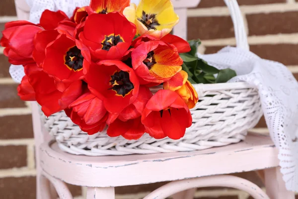 Bukiet kolorowych tulipanów w wiklinowym koszu, na krześle, na tle wnętrz domu — Zdjęcie stockowe