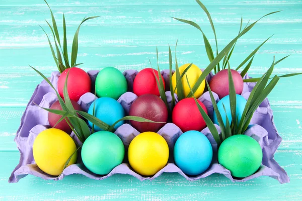 Colorful Easter eggs with grass in tray on wooden background — Stock Photo, Image