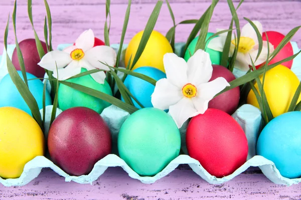 Ovos de Páscoa coloridos com grama e flores em bandeja no fundo de madeira — Fotografia de Stock