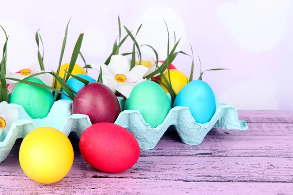 Colorful Easter eggs with grass and flowers in tray on table on bright background — Stock Photo, Image