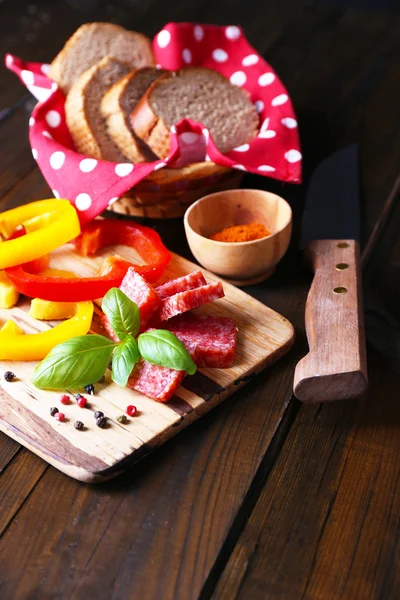 Composizione con coltello, saporita salsiccia di salame, pane e pepe a fette sul tagliere, su fondo di legno — Foto Stock