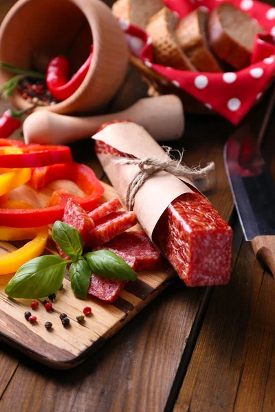 Composizione con coltello, saporita salsiccia di salame, pane e pepe a fette sul tagliere, su fondo di legno — Foto Stock