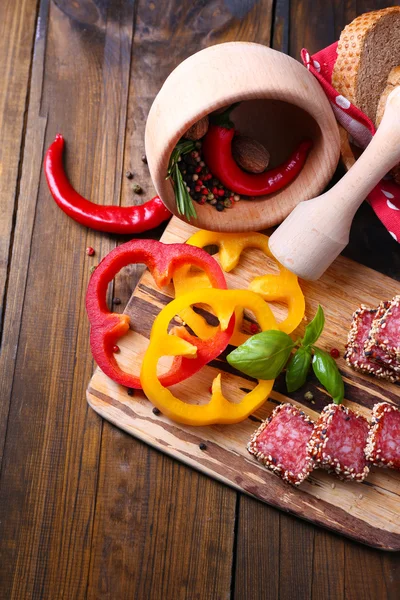 Composition of knife,    sliced salami sausage with sesame, on cutting board, on wooden background — Stock Photo, Image