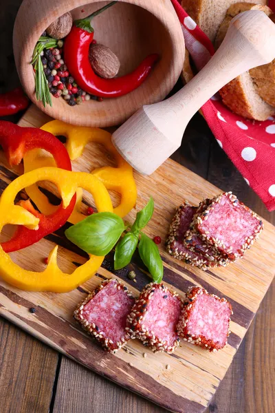 Samenstelling van mes, gesneden salami worst met sesam, op snijplank, op houten achtergrond — Stockfoto