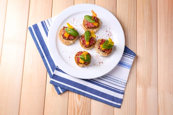 Tasty canapes with salami, pepper  and basil leaves, on plate, on wooden background — Stock Photo, Image