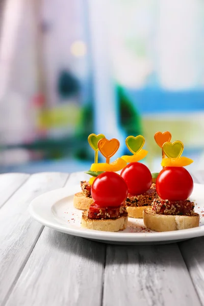 Välsmakande kanapéer med salami, tomat, paprika och basilika blad, på plattan, träbord, på ljus bakgrund — Stockfoto