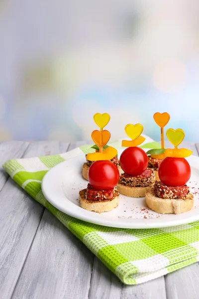 Leckere Canapes mit Salami, Tomate, Paprika und Basilikumblättern, auf Teller, auf Holztisch, auf hellem Hintergrund — Stockfoto