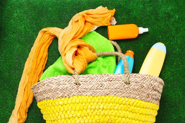 Wicker bag with colorful scarf, towel, bottles of lotions on  green background. — Stock Photo, Image