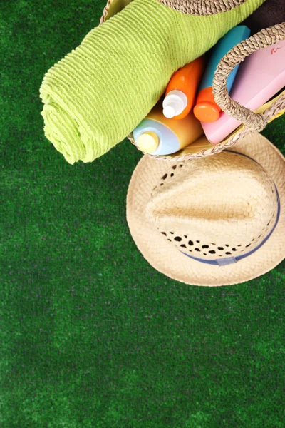 Wicker bag with colorful scarf, towel, bottles of lotions on  green background. — Stock Photo, Image