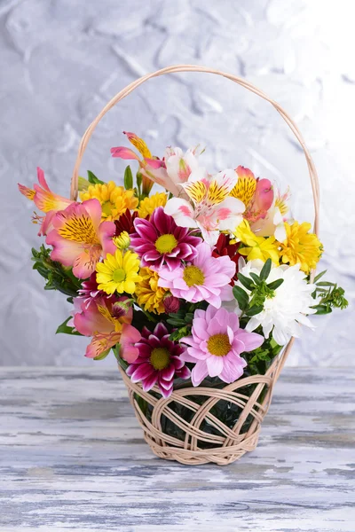 Belo buquê de flores brilhantes na cesta de vime na mesa no fundo cinza — Fotografia de Stock