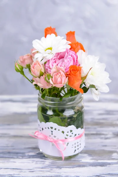 Beautiful bouquet of bright flowers in jar on table on grey background — Stock Photo, Image