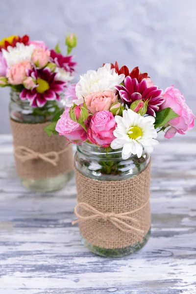 Hermoso ramo de flores brillantes en frascos sobre la mesa sobre fondo gris — Foto de Stock