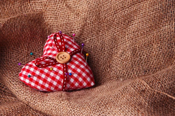 Ткань сердца с цветными булавками на мешковине фоне — стоковое фото