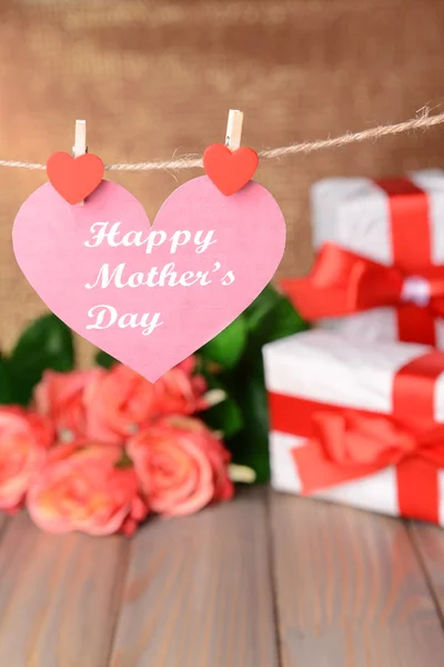 Gelukkig moeders dag bericht geschreven op papier hart met bloemen op bruine achtergrond — Stockfoto