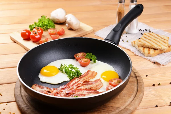 Huevos revueltos y tocino en la sartén en la mesa de cerca —  Fotos de Stock