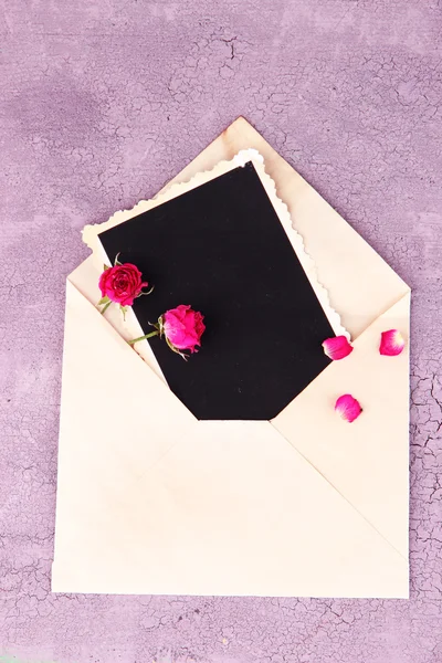 Sobre viejo con papel fotográfico en blanco y hermosas rosas secas rosadas sobre fondo de madera — Foto de Stock