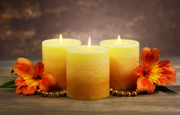 Belas velas com flores na mesa no fundo marrom — Fotografia de Stock