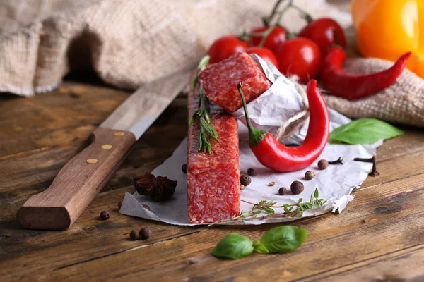 Tasty salami sausage and spices on wooden background — Stock Photo, Image