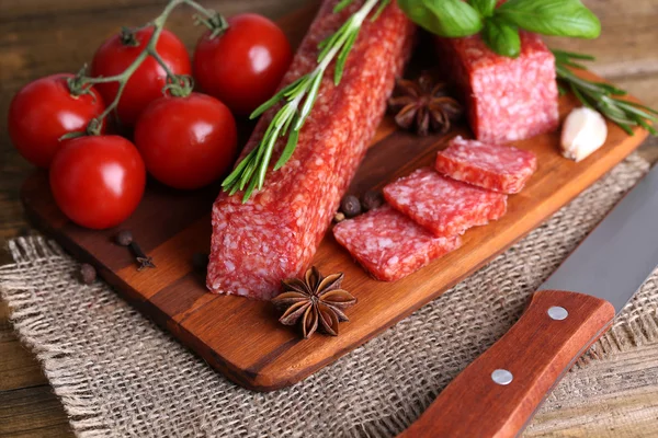 Tasty salami sausage and spices on wooden background — Stock Photo, Image