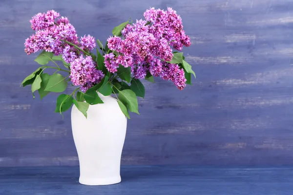 Beautiful lilac flowers in vase, on color wooden background — Stock Photo, Image