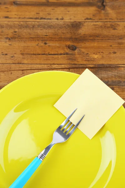 Пустая бумага, прикрепленная к вилке, на тарелке, на цветном деревянном фоне — стоковое фото