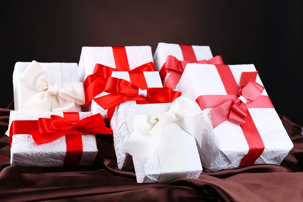 Beautiful gifts with red ribbons on silk, on dark background — Stock Photo, Image