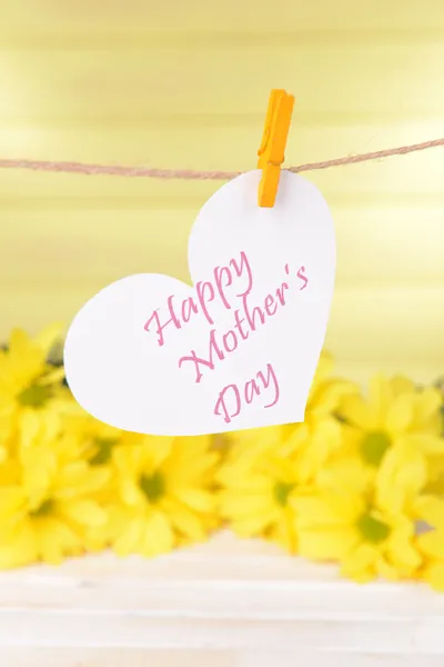 Gelukkig moeders dag bericht geschreven op papier hart met bloemen op gele achtergrond — Stockfoto