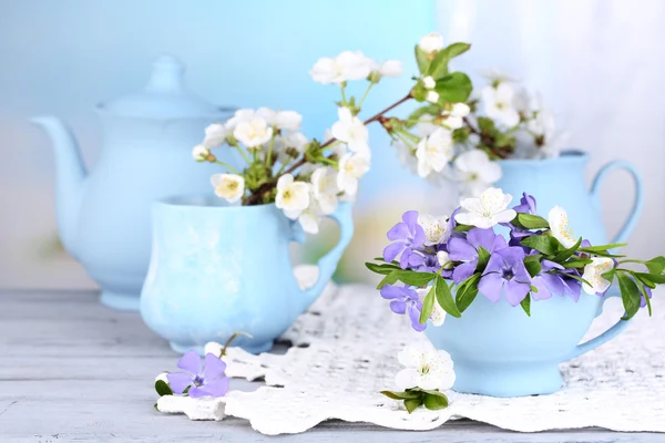 Beautiful spring flowers in cups on wooden table — Stock Photo, Image