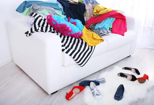 Rommelig kleurrijke kleding op sofa op lichte achtergrond — Stockfoto