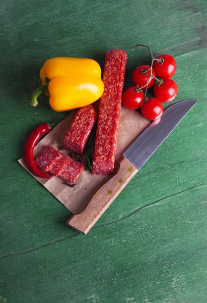 Salsicha de salame saboroso, legumes e especiarias sobre papel fundo de madeira — Fotografia de Stock