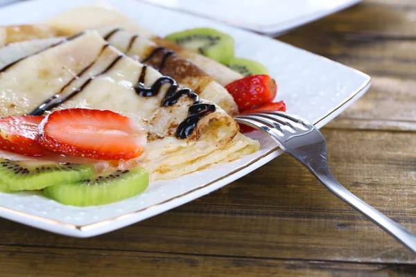 Heerlijke pannenkoeken met aardbeien en chocolade op plaat op tafel — Stockfoto