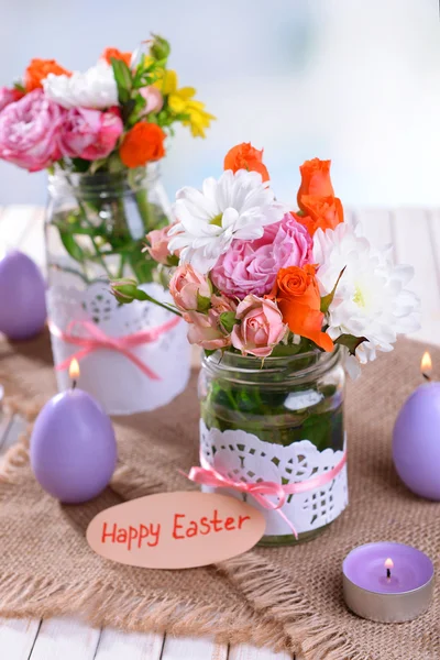 Beautiful bouquet of bright flowers in jars on table on light background — Stock Photo, Image