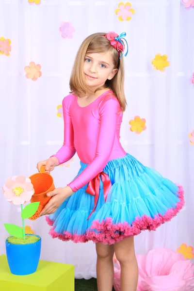 Hermosa niña pequeña en falda pequeña regando flores sobre fondo decorativo —  Fotos de Stock