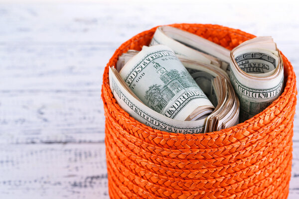 Пачки долларов хранятся в корзине на деревянном столе
