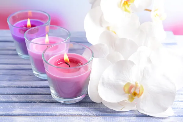 Hermosas velas de colores y flores de orquídea, sobre mesa de madera de color, sobre fondo claro —  Fotos de Stock